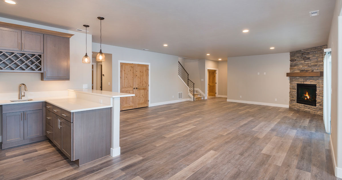 Modern basement renovation featuring a kitchenette, stone fireplace, and wood flooring.