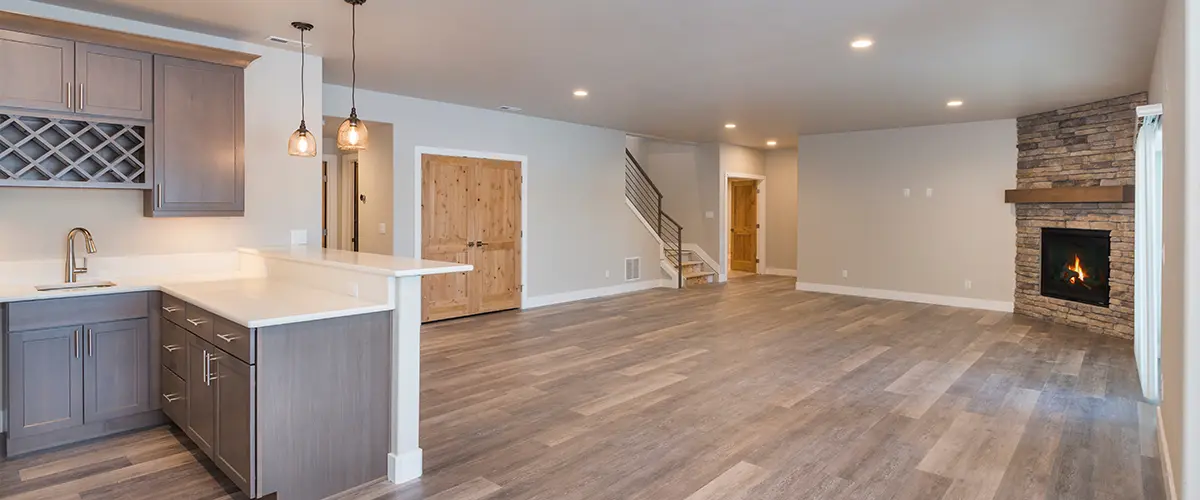 Modern basement renovation featuring a kitchenette, stone fireplace, and wood flooring.